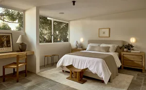 The bedroom features a modern minimalistic design with a wooden bedframe and lamp, complemented by a white rug and a large wi