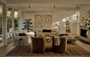 A modern interior living room featuring neutral textiles and earth tones, with a fireplace, sofas, armchairs, and large artwo