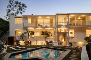 A modern residential house featuring concrete and glass materials with a pool in the foreground.