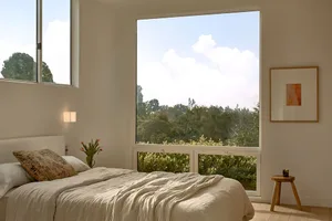 A modern bedroom with textured bedding and a large window overlooking greenery.