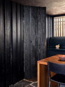 A modern kitchen with charred-wood walls and a wooden table.