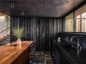 Industrial-inspired kitchen featuring black marble countertops, charred wood accents, and a stone floor.