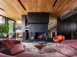 A spacious, industrial-style living room featuring a prominent, modern fireplace made of black slate tiles, surrounded by pin