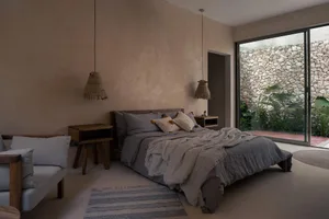 Minimalist bedroom with concrete walls and floor, featuring a bed with gray bedding and minimalistic decor.