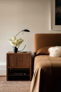 A minimalist bedroom featuring a wooden side table adorned with a vase of white flowers.