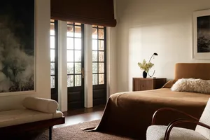 A minimalist bedroom with a wooden headboard, brown carpet, and a white armchair.