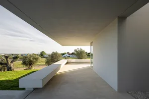 A minimalist interior design featuring concrete and stone materials, with a view of a rural landscape.