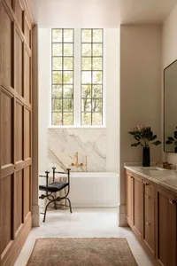Minimalist bathroom featuring a freestanding marble bathtub with a wooden vanity and large tall window.
