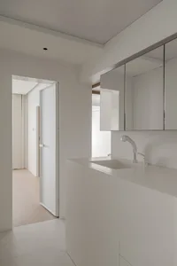 A minimalist white bathroom with a single sink, mirror, and cabinet.