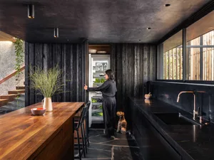 A modern residential kitchen with black stone countertops, wooden cabinetry, and stainless steel appliances.