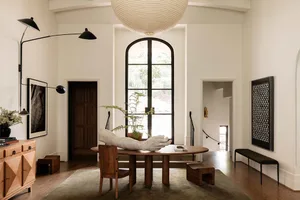 A modern living room featuring a wooden table, stone wall, and large arched window.
