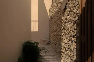 A narrow stone-walled hallway with a plant and sunlight coming through a window.