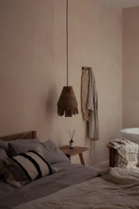 A minimalist bedroom featuring textile accents, wooden elements, and a wicker lampshade.