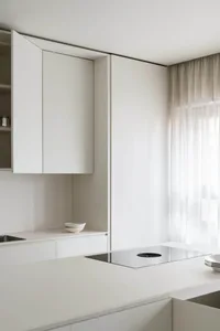 Modern minimalist white kitchen with glass cabinets and stainless steel appliances.