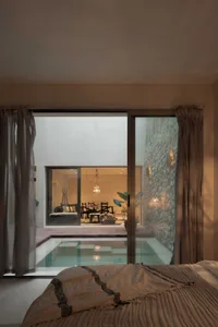 A modern bedroom with a concrete wall, a plunge pool, and a see-through glass wall that leads to a living area with a stone w