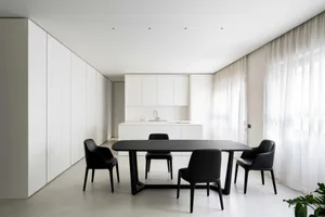 A modern minimalist kitchen and dining space with white cabinets, black furniture, and sheer curtains.