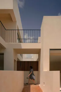 Person walking through a modern residential exterior featuring sandstone, concrete, and glass materials.