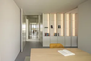A minimalist office space featuring a metal and glass bookshelf with integrated lighting.