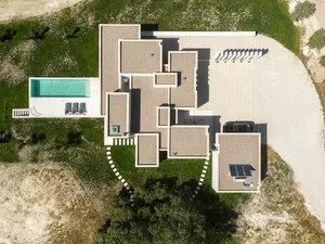 Aerial view of a minimalist modern house featuring concrete and glass materials, with a large swimming pool and a spacious dr