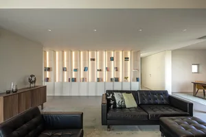 A modern living room with a black leather sofa, illuminated shelves, and minimalist decor.