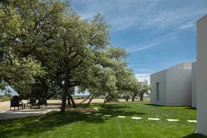 A modern residential building with a concrete exterior and a well-maintained garden under a clear blue sky.