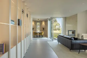 A modern living room with a concrete fireplace and black leather sofas, featuring minimalistic design and natural light.