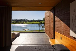 A minimalist bedroom featuring a black bedspread and a wooden headboard, with a view of a lake.