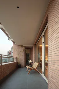 A modern balcony with brick walls, glass doors, and a wooden chair.