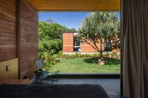 Modern bedroom featuring a large window with a view of a palm tree and a well-maintained lawn.