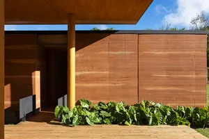 A modern exterior space featuring wooden architecture with green plants and a blue sky in the background.