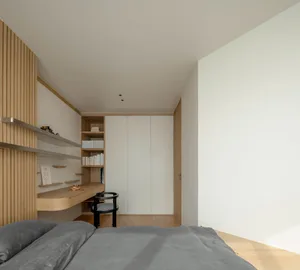 A minimalist bedroom with wooden and metallic elements, including a bed, shelves, and a closet.