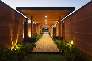 A modern retail storefront with wooden walls and led lighting at dusk, featuring lush foliage along the sides of the pathway.