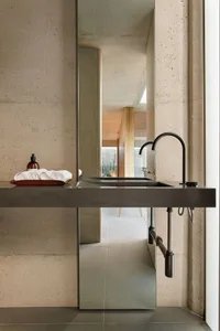 Modern minimalist bathroom with concrete walls and floor, featuring a long sink with a black faucet and a large mirror above.