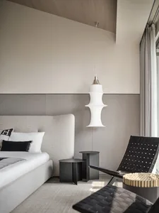 Modern minimalist bedroom featuring fabric upholstered furniture, metal accents, and glass pendant light hanging from the cei