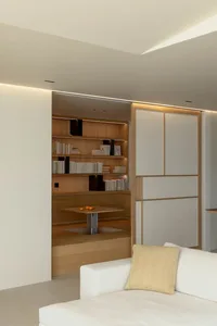 A modern minimalist living room featuring a white couch, a wood coffee table, and a bookshelf filled with books.