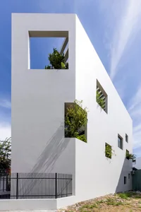 A modern, exterior view of a white-box house with concrete walls and large windows.