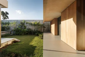 A modern hallway features a concrete wall, wooden walkway, and lush greenery.