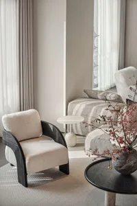 A modern living room with a white fabric armchair, a marble side table, and a wooden coffee table. The room features a sofa w