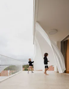 Two children playing with a white cloth on a tiled balcony with a white railing.