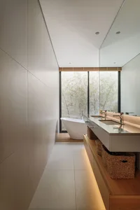 A modern minimalist bathroom interior with white polished concrete walls, a white bathtub, a floating vanity with a dual sink
