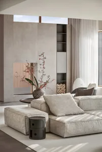 A modern minimalist living room with a concrete fireplace, fabric furniture, and glass shelves.