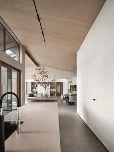 A modern minimalist kitchen with concrete walls, a wooden island, and a large window providing natural light.