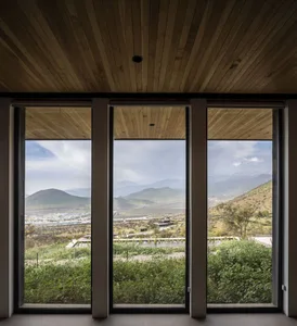 A modern minimalist residential interior featuring large windows with a view of the mountains and lush green landscape.