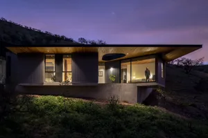 Modern residential house exterior during twilight with wooden and concrete exterior and large glass windows.