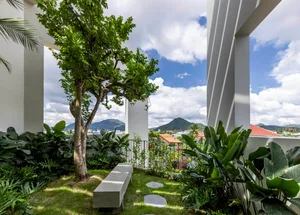 Concrete patio surrounded by lush green plants against a backdrop of mountains under a cloudy sky.