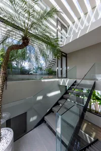 Modern staircase with glass railings and palm tree in indoor courtyard.