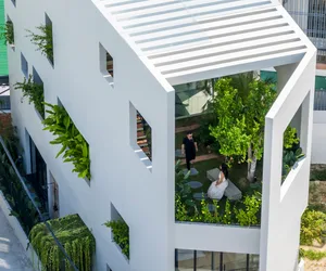 A modern, white building with green plants on the windows and lush greenery surrounding it.