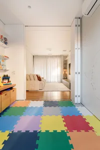 A colorful playroom with a geometric pattern on the floor, white walls, and a tan sofa with red and brown pillows.