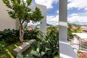 A minimalist residential patio featuring concrete structures and lush greenery, with a view of mountains in the distance.