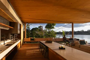 A modern living room with a large outdoor area overlooking a lake, featuring a wooden ceiling, a kitchen with an island, and 